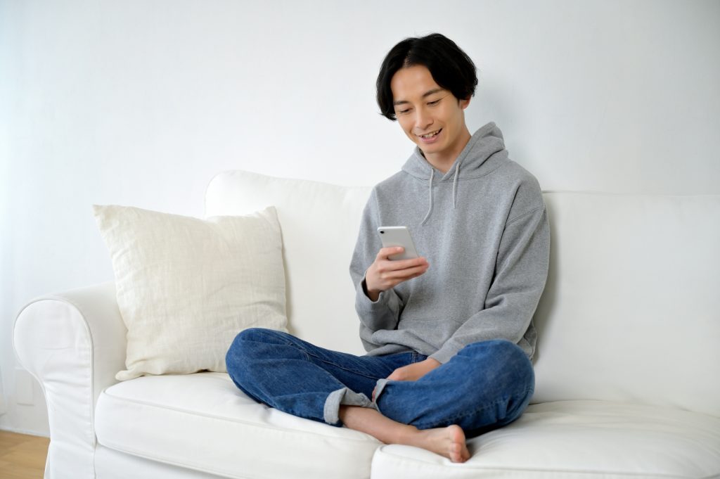 ソファーに座ってスマホを使う男性の様子