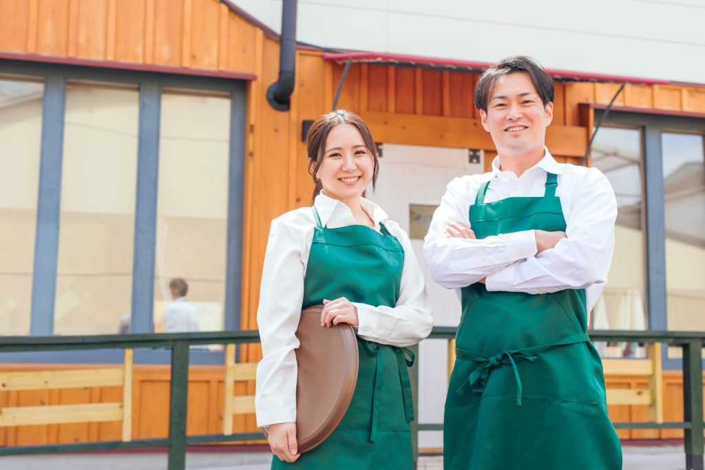 お店の前に立つエプロン姿の男女の様子